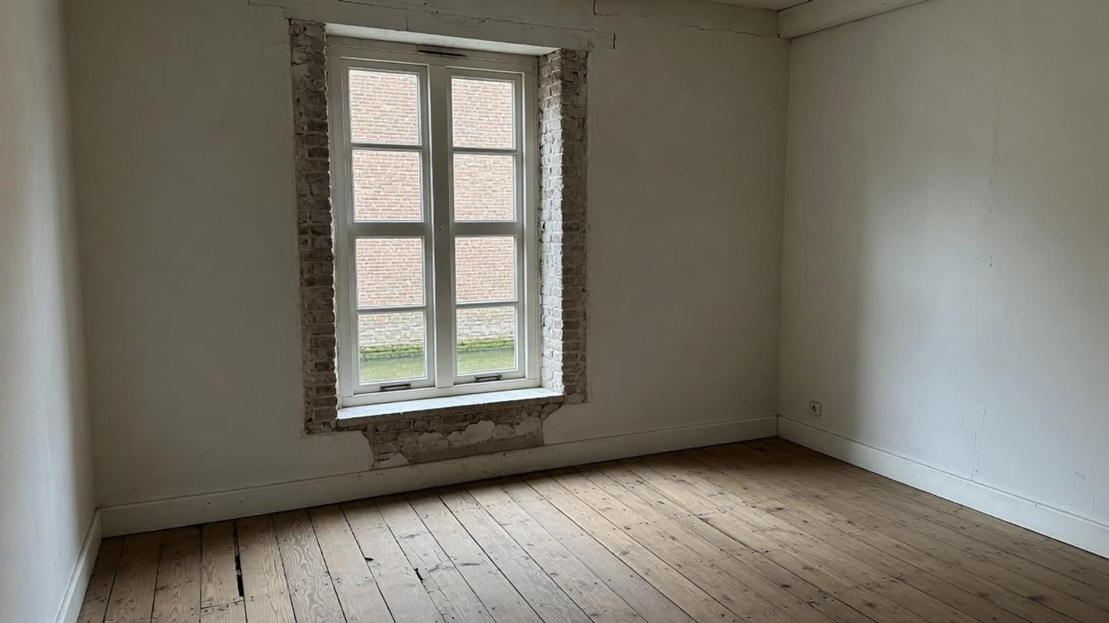 Lege kamer met een diep raamkozijn in dik metselwerk en kale vloerdelen