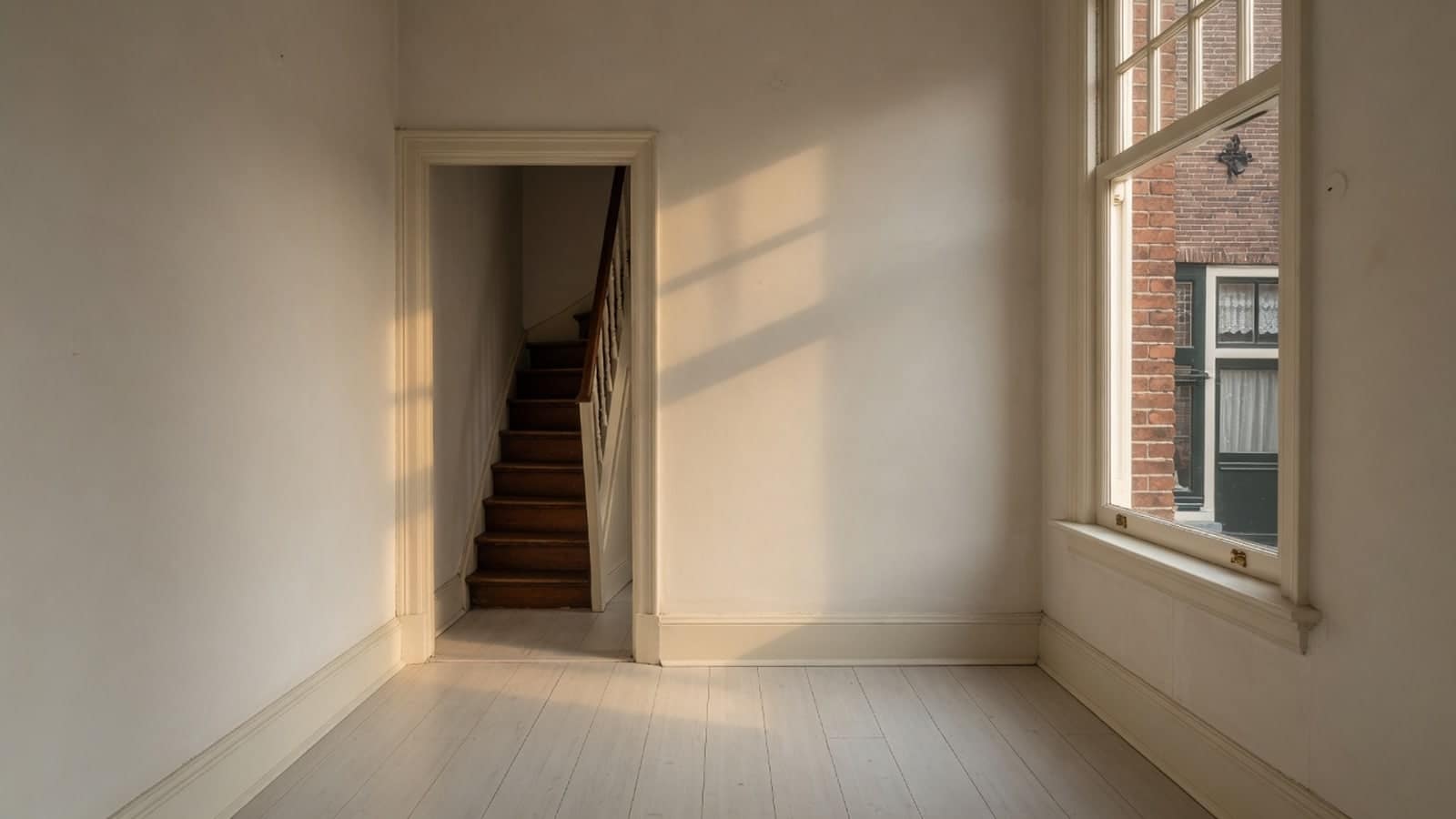 Leeggehaalde bovenkamer in laag namiddaglicht, met een trap door de deuropening
