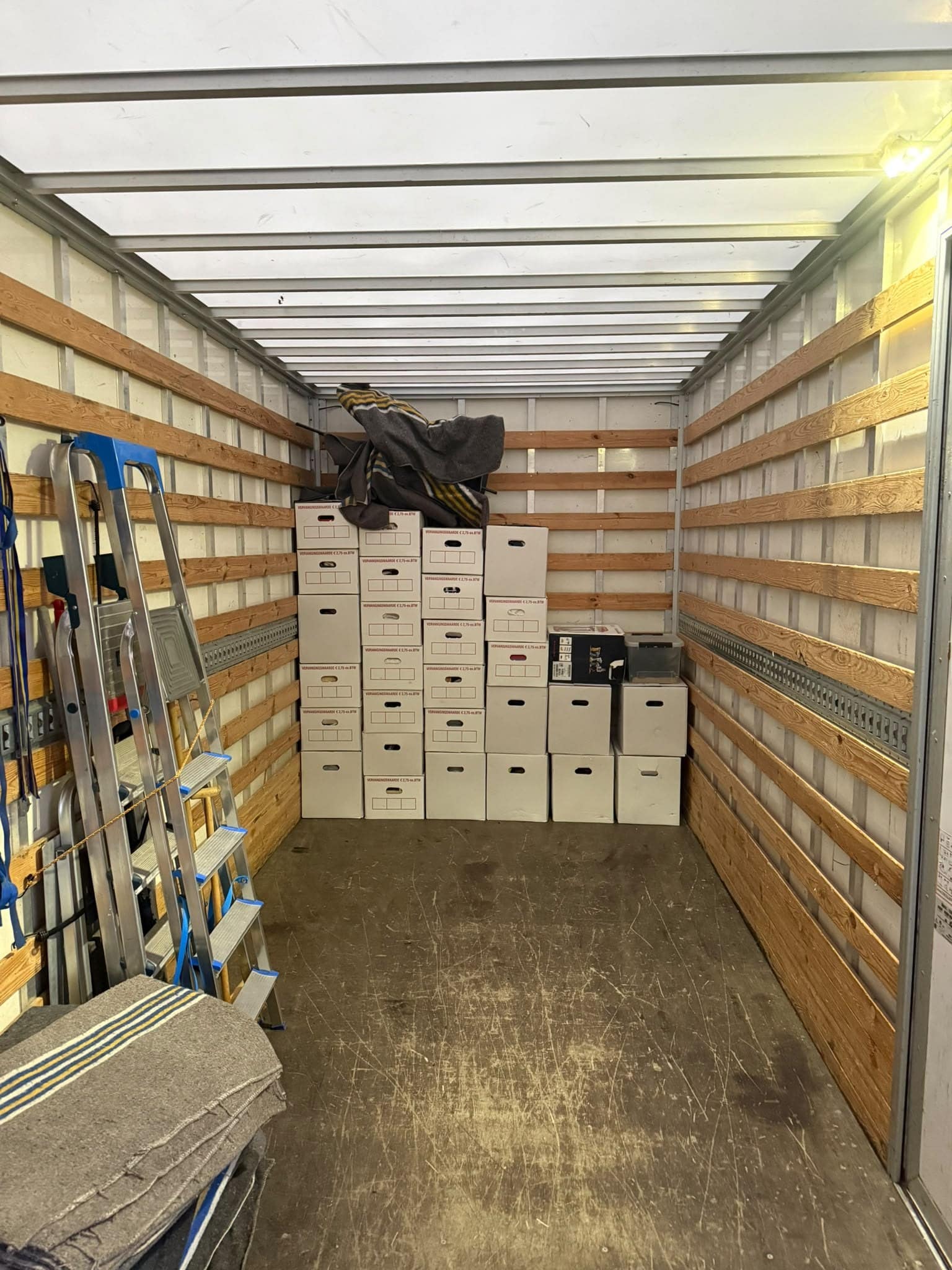 Archiefdozen in gelijke stapels tegen de kopwand van een laadbak, met een trap ernaast
