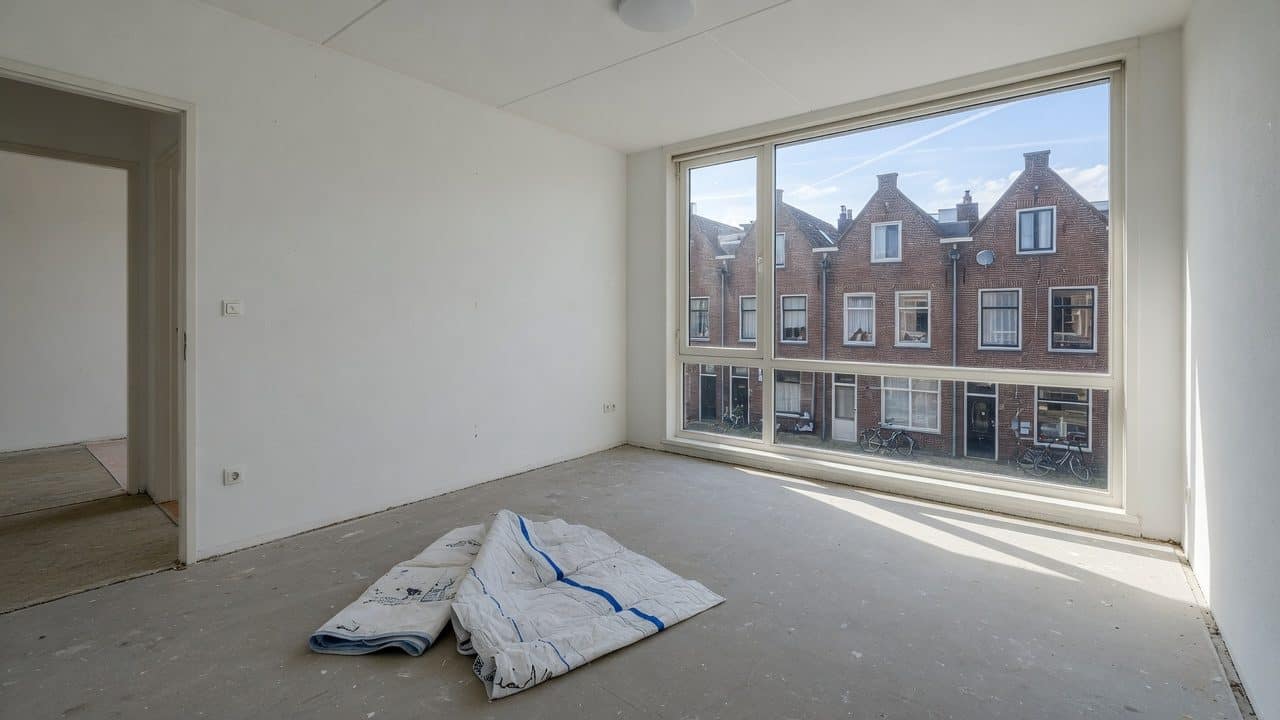 Kale dekvloer zonder vloerbedekking, een opgevouwen beschermdeken en zicht op Nederlandse gevels