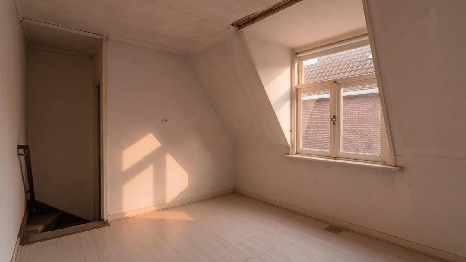 Lege zolderkamer met schuin dak, met de zon door de dakkapel