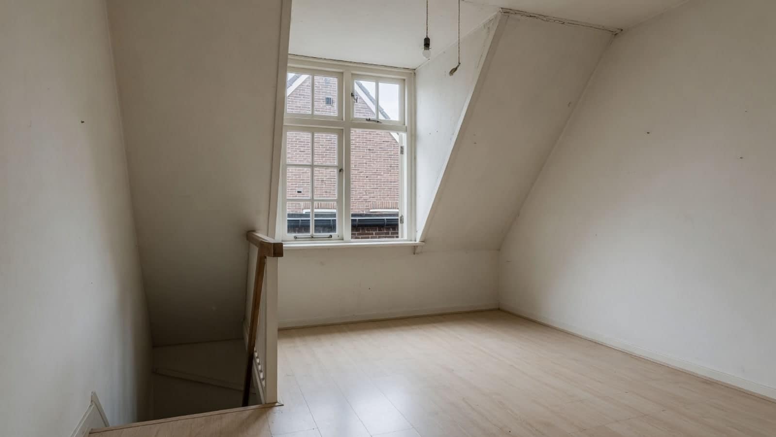Lege zolderkamer met schuin dak en een dakkapel, bereikbaar via een steile trap