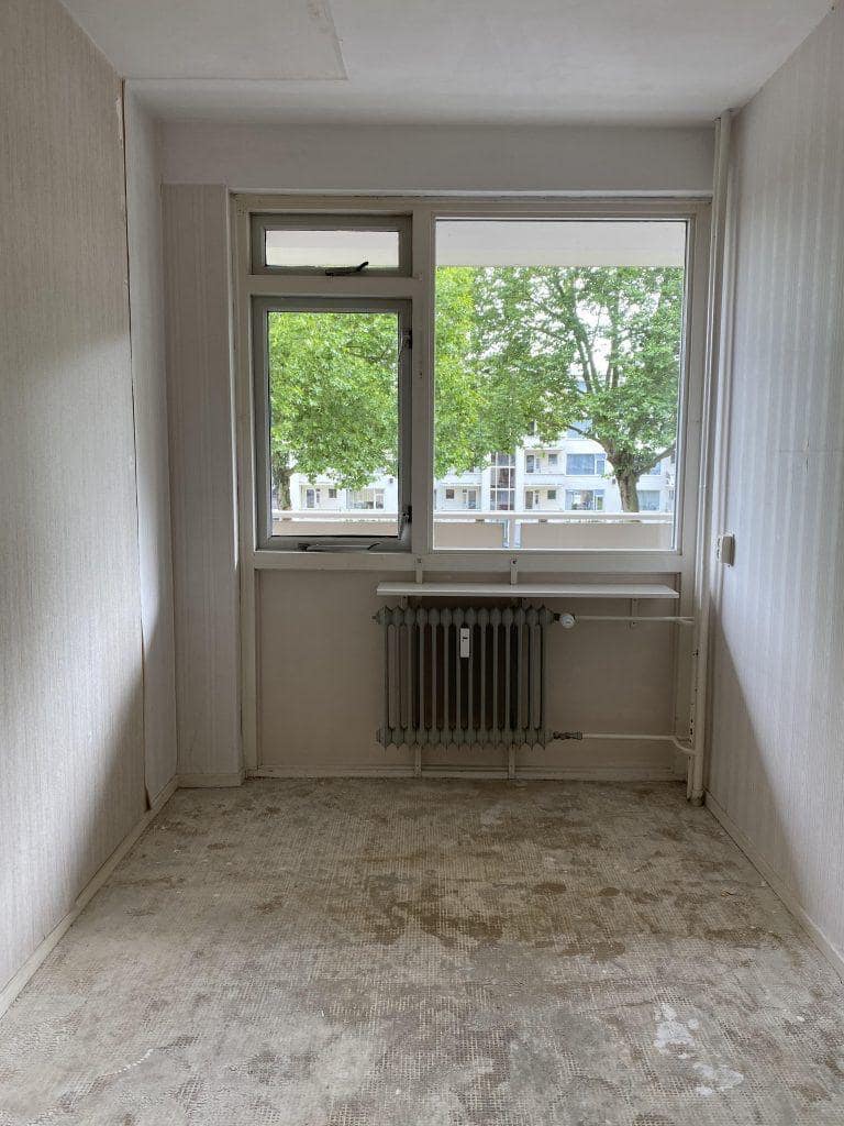 Leeggehaalde kamer met kale ondervloer en een vensterbankplank onder het raam