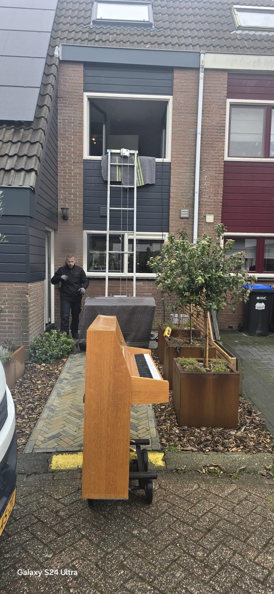 Piano die met een ladderlift naar een raam op de eerste verdieping gaat