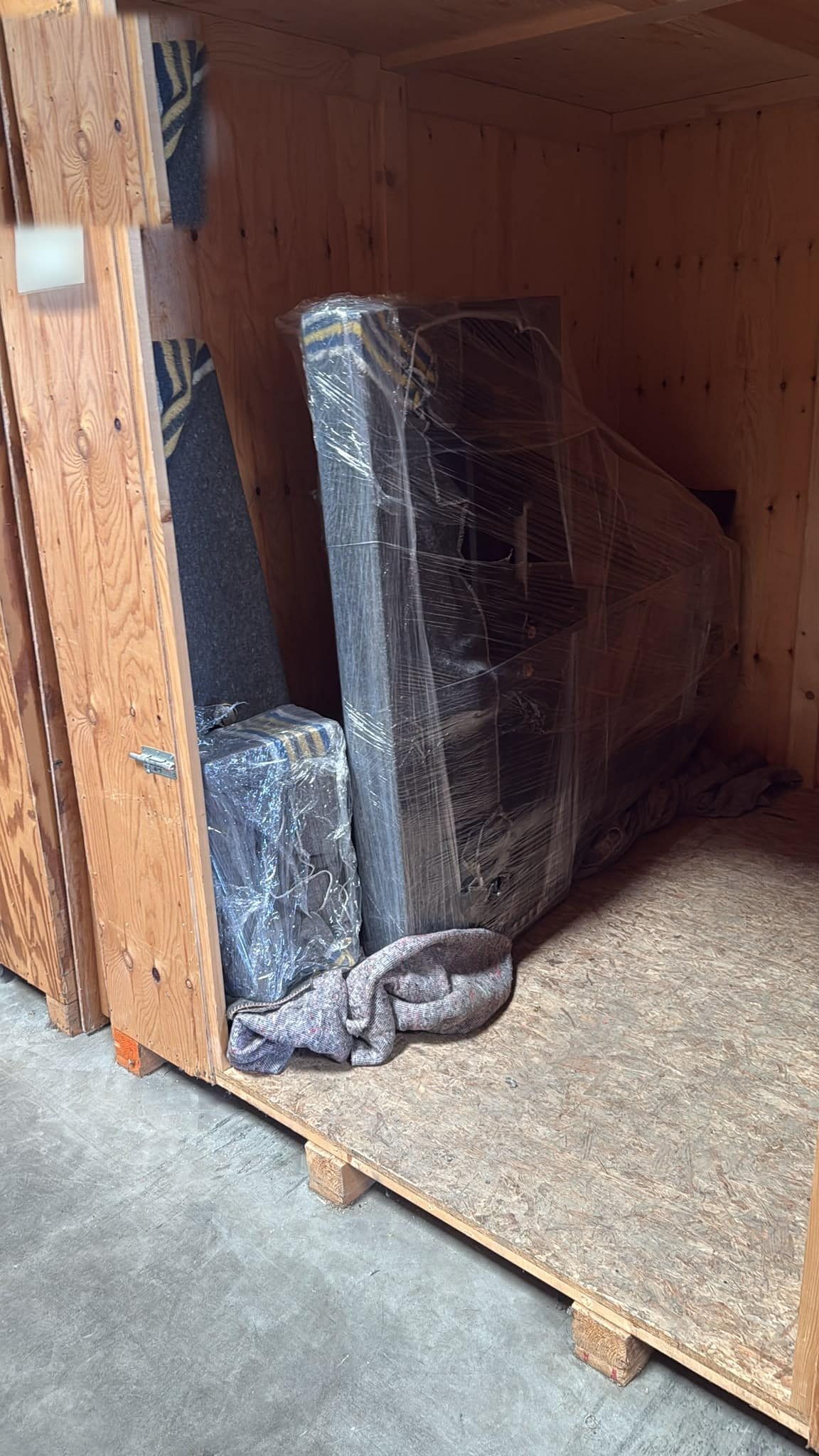 Ingepakte piano in een houten opslagkist, op dekens en tegen de wand