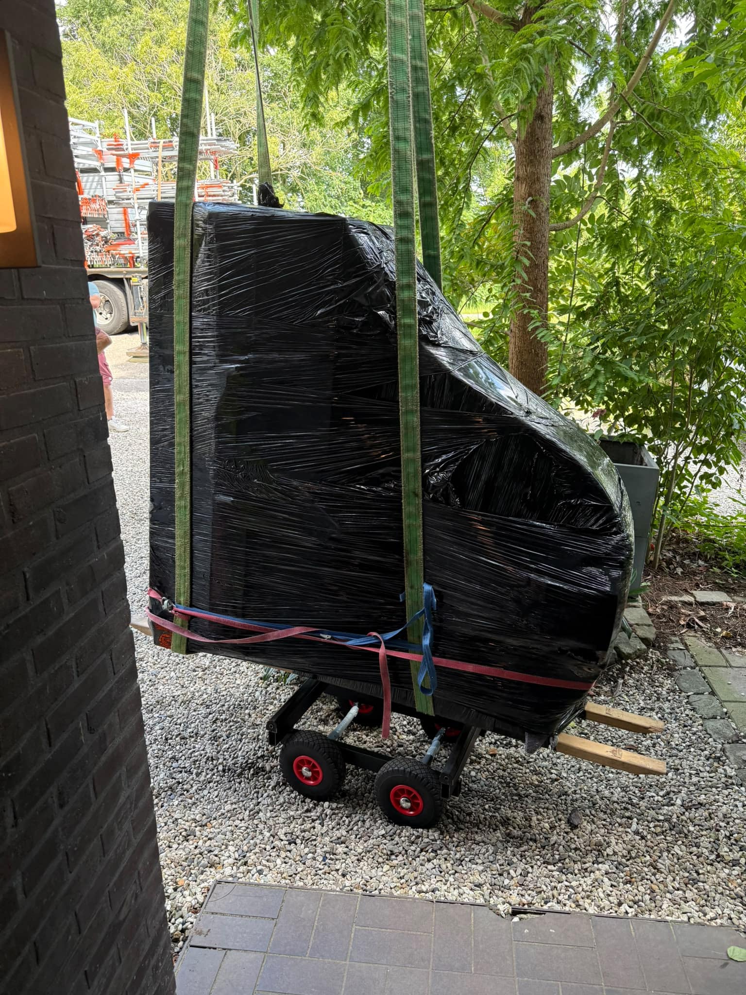 Ingepakte piano aan spanbanden, hangend aan de takel boven een pianowagen