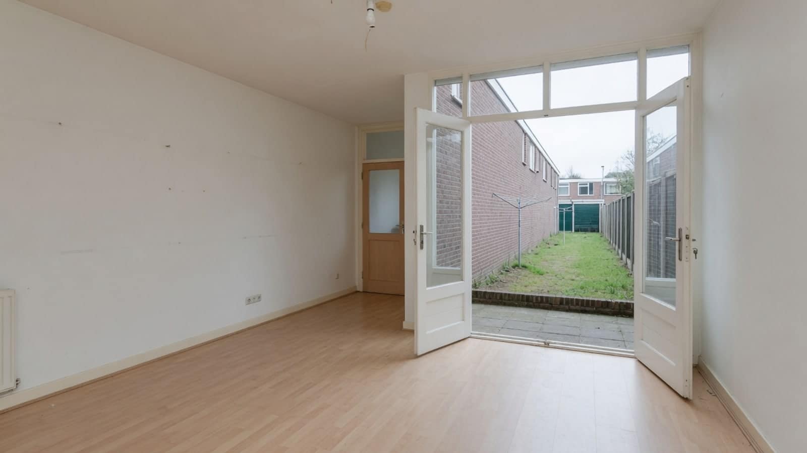 Lege woonkamer met openslaande deuren naar een lange smalle achtertuin