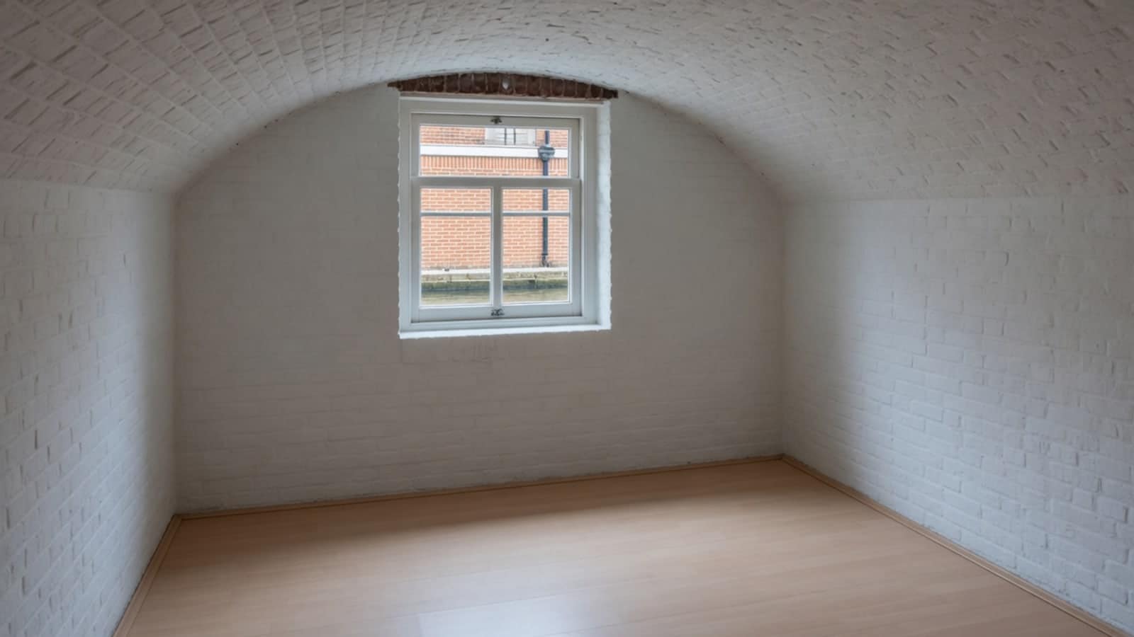Leeg gewelfd kelderruim van witgeschilderd metselwerk met een klein diep raam